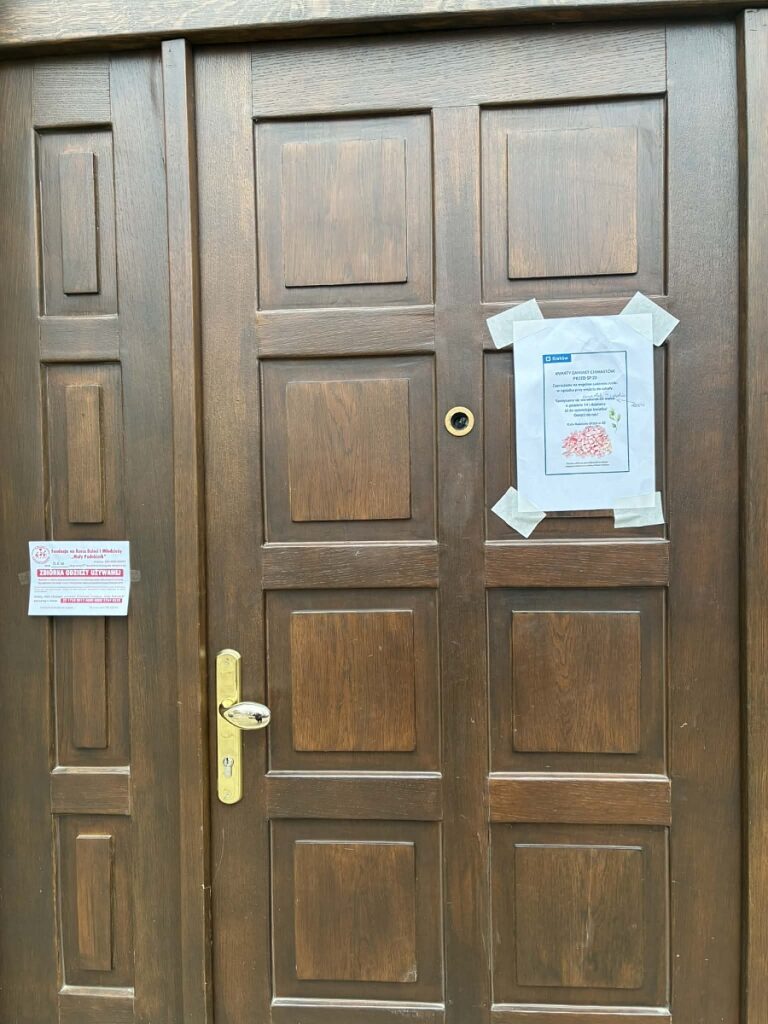 Drzwi kamienicy na ul. Chmielowskiego, na których wisi plakat z ogłoszeniem o akcji sadzenia kwiatów w ramach Inicjatywy Lokalnej.