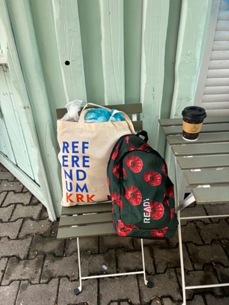 Plac na stawach w krakowie, plecak i torba z napisem referendum lezace na krzesle. Na plecaku napis "Ready". Obok na stoliku stoi kubek z kawą